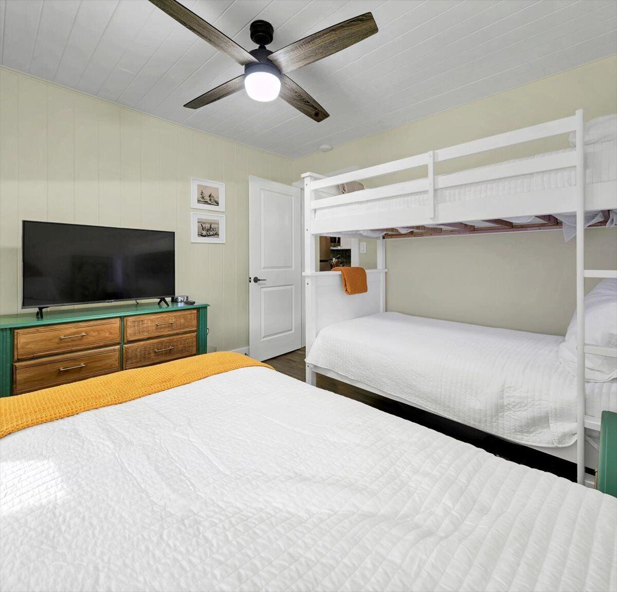 A room with bunk beds, a television, a dresser, and a ceiling fan.