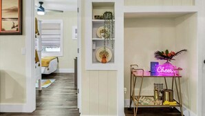 A hallway with a wooden floor, a white door, a ceiling fan, and a neon sign that says "Cheers". - Safety Harbor Motel (Safety Harbor)