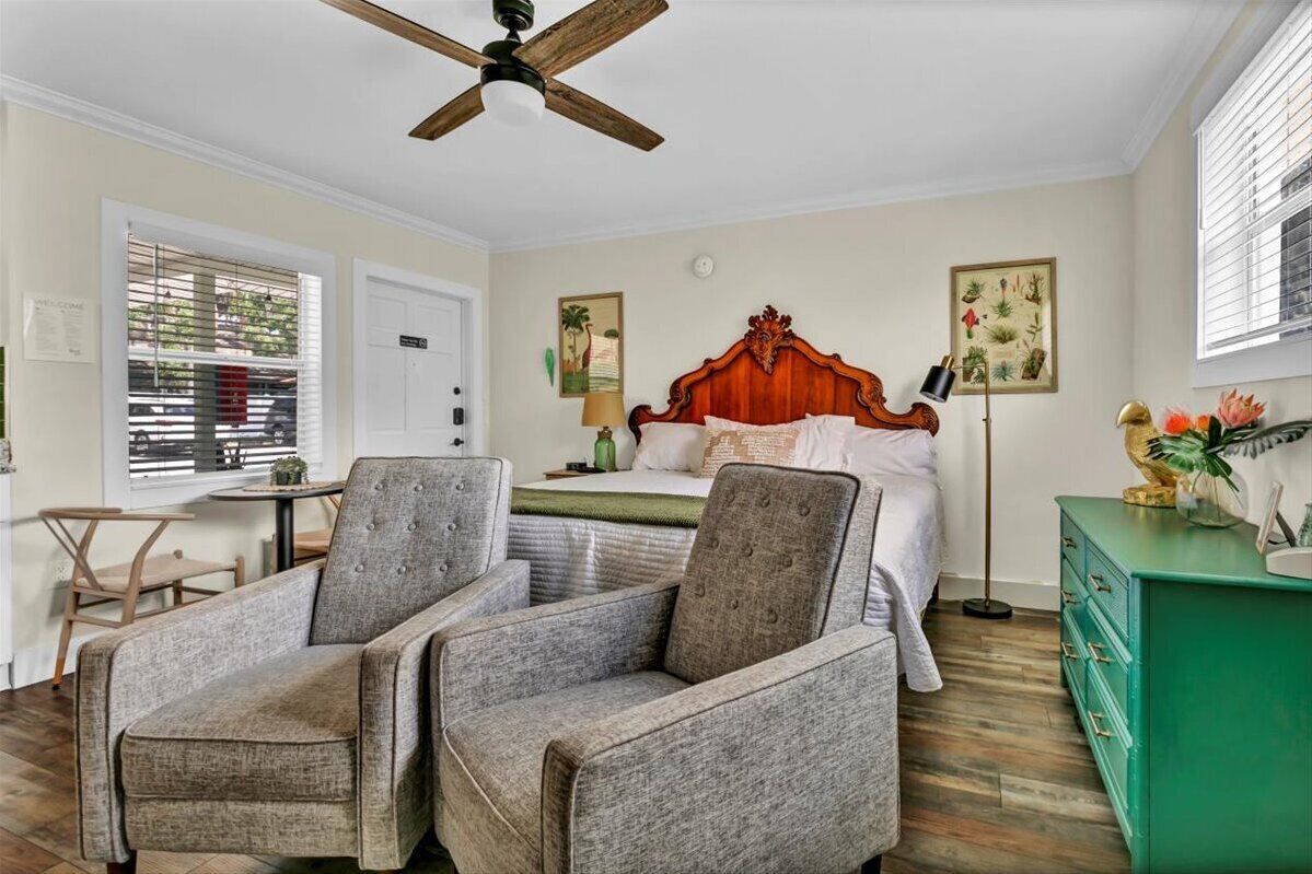 A bedroom with a wooden bed, two grey armchairs, a green dresser, and a ceiling fan.