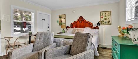A bedroom with a wooden bed, two grey armchairs, a green dresser, and a ceiling fan.