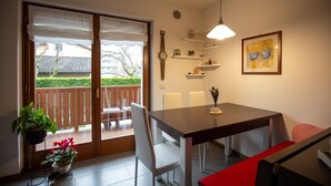 A dining area with a table, chairs, a clock, shelves with items, and a view through a glass door. - Casa Shiva - Belvedere Dolomiti (Sedico)