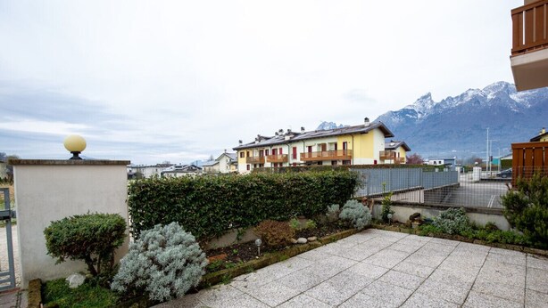 A residential area with a paved courtyard, a hedge, and a view of houses and mountains in the background. - Casa Shiva - Belvedere Dolomiti (Sedico)