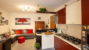 A compact kitchen with a central island, a dining area with a sofa, and a living room with a bookshelf. - Casa Shiva - Belvedere Dolomiti (Sedico)