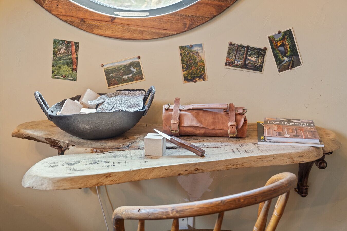 A rustic wooden table with a bowl, a leather bag, a book, and a chair.