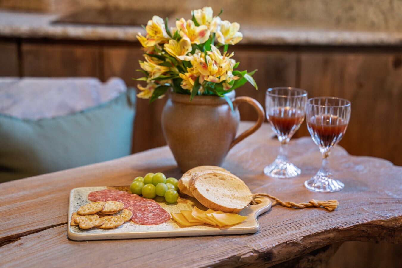 Une table en bois sur laquelle on a disposé une planche de charcuterie, un vase de fleurs et deux verres de vin rouge.