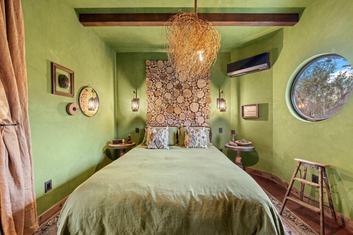 Ein Zimmer mit einem Bett, einem Wandbild aus Holzscheiten, einem runden Spiegel und einer Leiter.