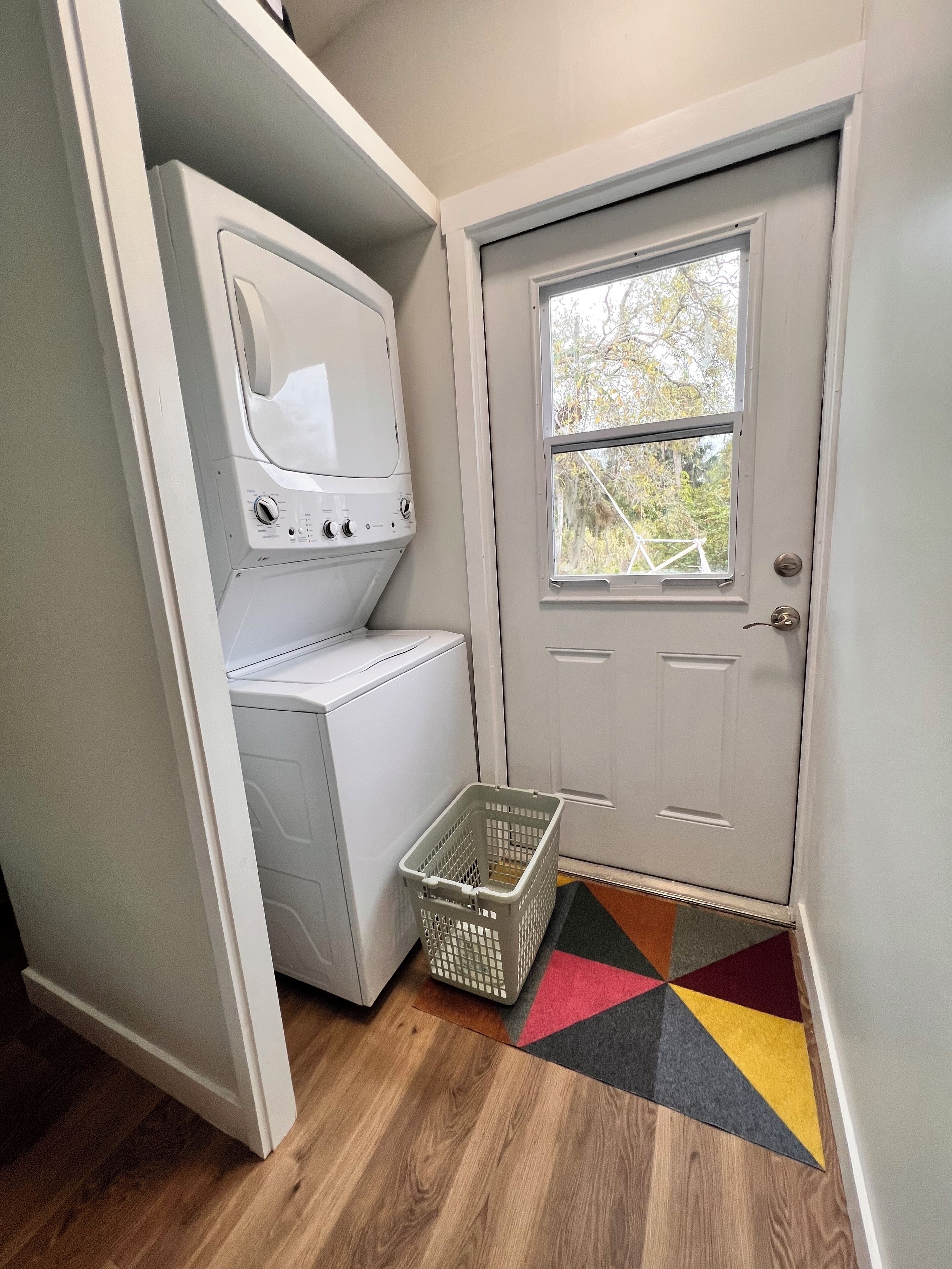 A laundry room with stacked washers and dryers, a basket, and a door with a window.