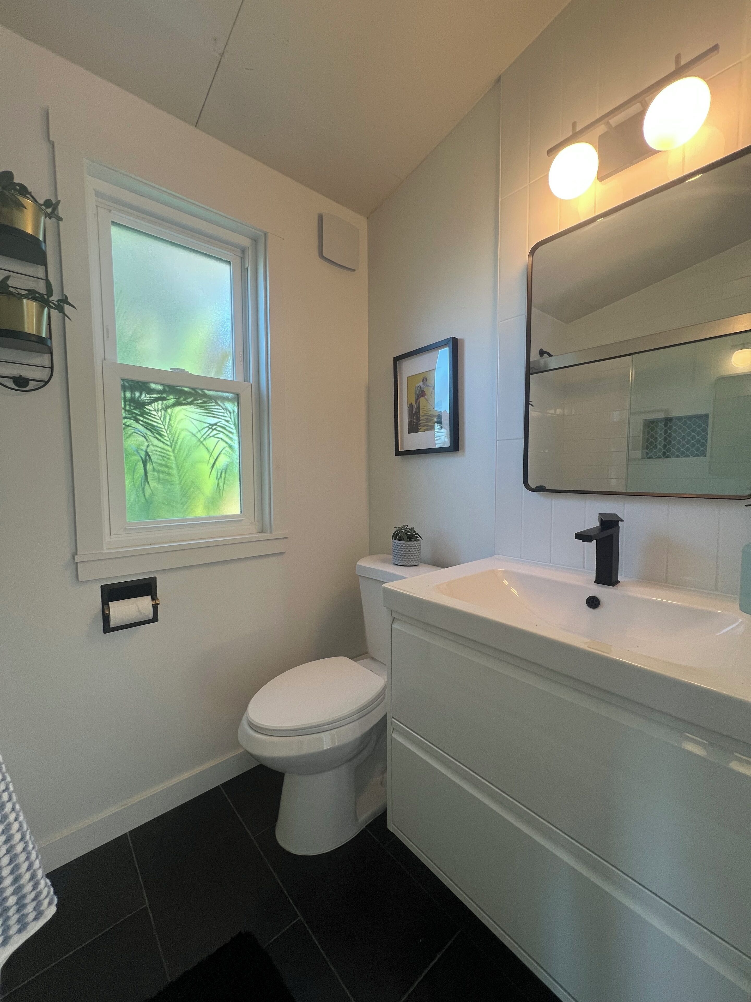 Une salle de bain équipée de toilettes, d’un lavabo et d’une fenêtre donnant sur un espace verdoyant.