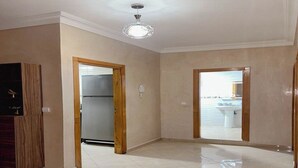 A spacious room with a tiled floor, a wooden door, and a ceiling light fixture. - Cosy apartment near the airport (Marrakech)