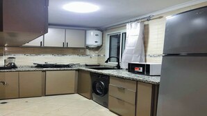 A compact kitchen with a washing machine, a microwave, and a refrigerator. - Cosy apartment near the airport (Marrakech)
