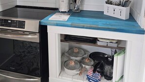 Una cocina moderna con estufa, horno y campana extractora de acero inoxidable. Hay estantes arriba con vajilla y un botiquín de especias abajo con utensilios.