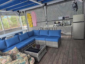 Un espace extérieur aménagé avec un coin salon abrité, comprenant un canapé bleu, des meubles en osier et une petite table.
