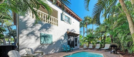 A poolside area with a white building, palm trees, and outdoor furniture.