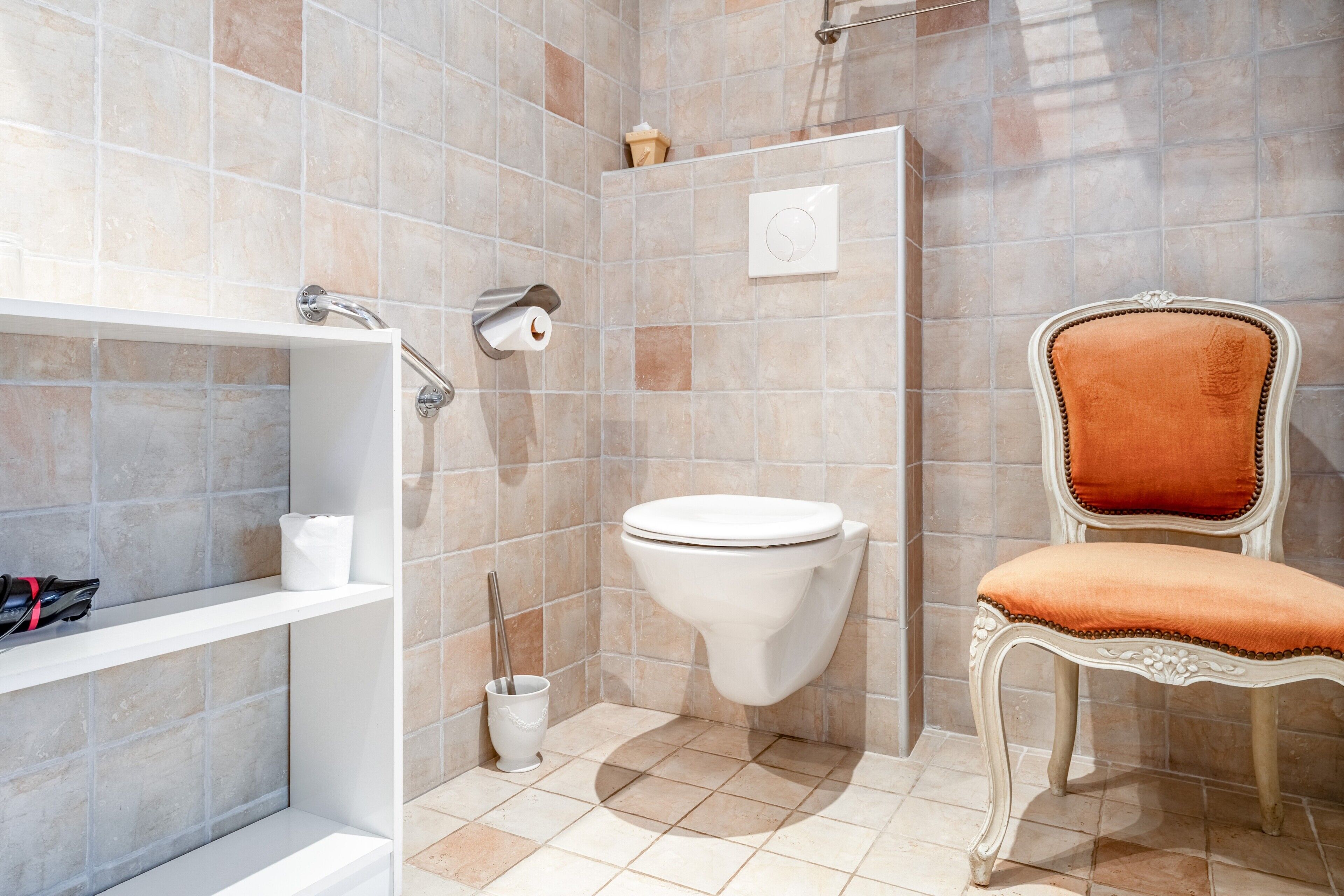 Un baño con inodoro, ducha, tocador con perchero y una silla.