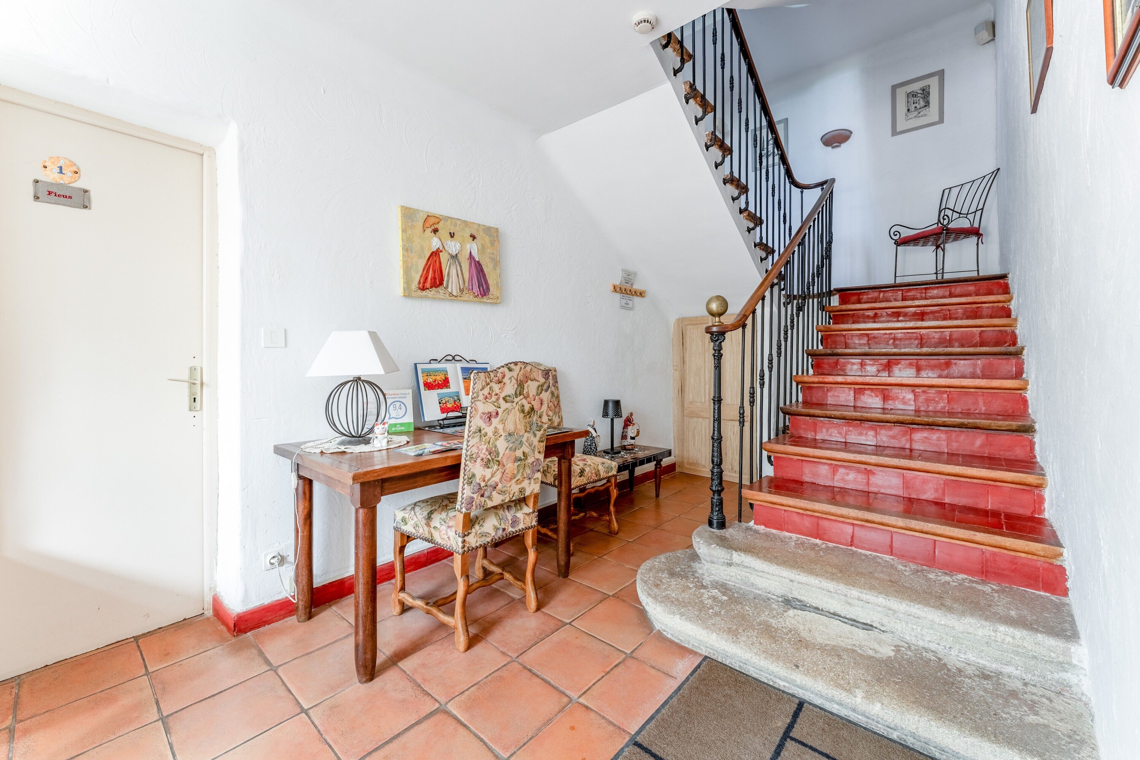 Una escalera con peldaños rojos, una silla de madera, una mesa con una lámpara y un cuadro en la pared.