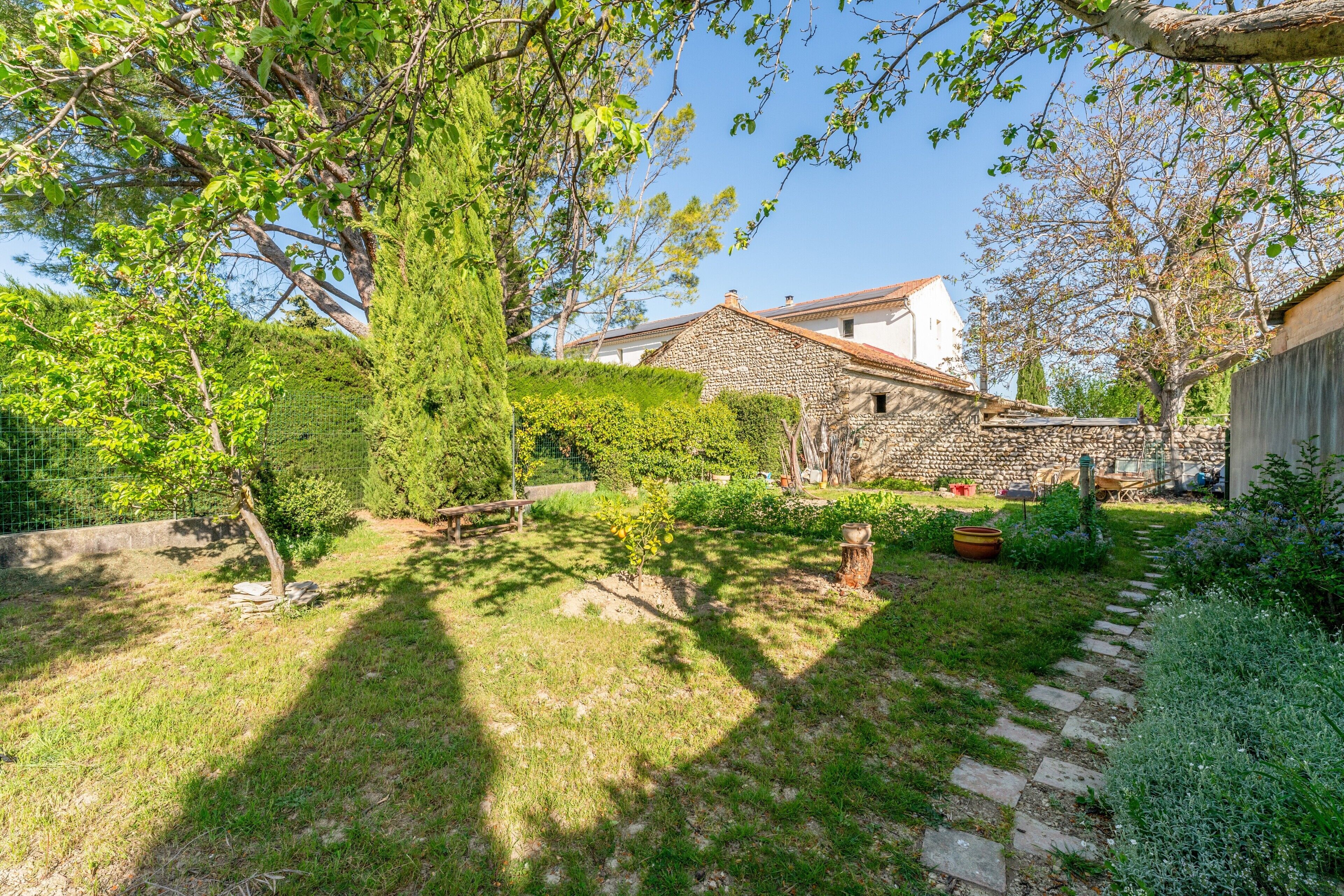 Ein Gebäude aus Stein mit einem Ziegeldach, umgeben von einem Garten mit einem Pflasterweg und einem umfriedeten Bereich.