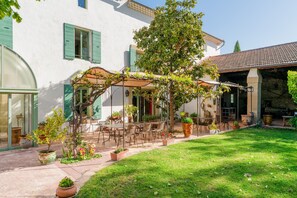 A courtyard with outdoor seating, potted plants, and a building with green shutters. - Mas de Bouvau: Room 3 Rosa, Wi-Fi and Air Conditioning (Violès)