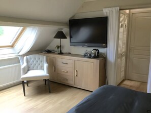 A room with a bed, a desk with a lamp, a TV, and a window with curtains.