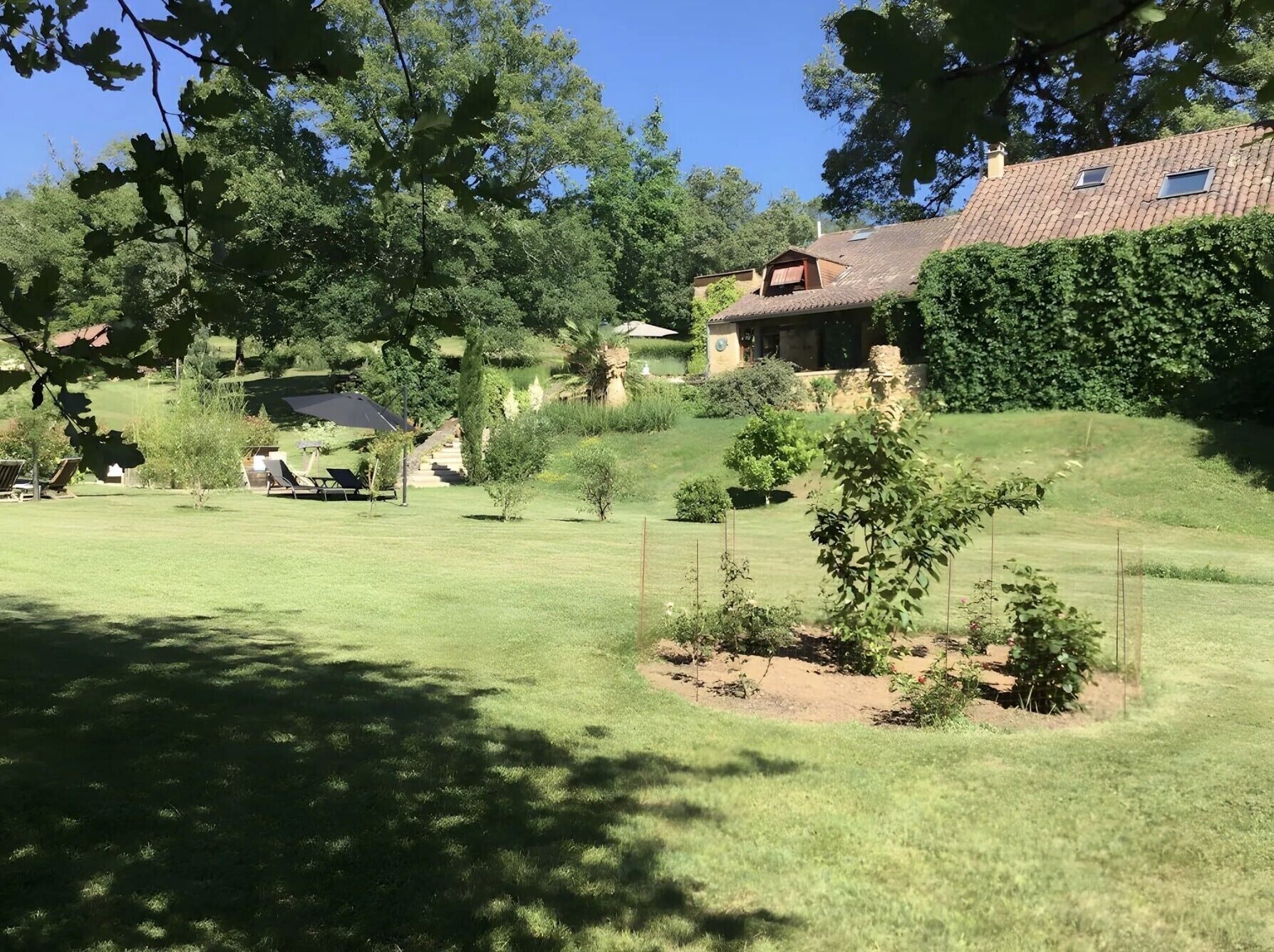 Een woonhuis met een verzorgd gazon, een kleine tuin en een gebouw met pannendak.