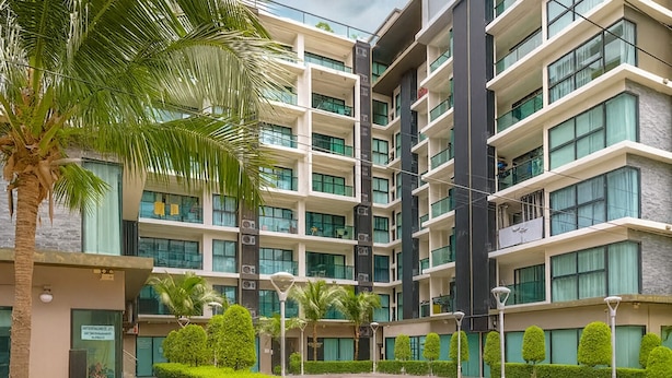 A multi-story residential building with a modern architectural design, featuring balconies, large windows, and a landscaped courtyard with palm trees and neatly trimmed bushes. - Cozy 2 Bedroom Condo in Pratumnak (Muang Pattaya)