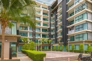 A multi-story residential building with a modern architectural design, featuring balconies, large windows, and a landscaped courtyard with palm trees and neatly trimmed bushes. - Cozy 2 Bedroom Condo in Pratumnak (Muang Pattaya)