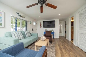 Un salon comprenant un canapé, des fauteuils, une table basse, un téléviseur et un ventilateur de plafond.