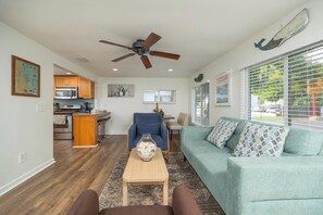 A living room with a sofa, a coffee table, and a dining area with a kitchen in the background.