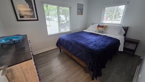 A bedroom with a bed, two windows with blinds, a wooden dresser, and a framed picture on the wall.