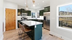 A modern kitchen with dark green cabinets, a white island, stainless steel appliances, and pendant lighting. - HotTub+Sauna+Garage+DeerValleyEast+Jordanelle (Heber City)