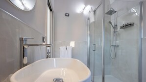 Un baño moderno con un lavamanos grande de color blanco, una ducha con mampara de vidrio y un espejo con luz integrada.