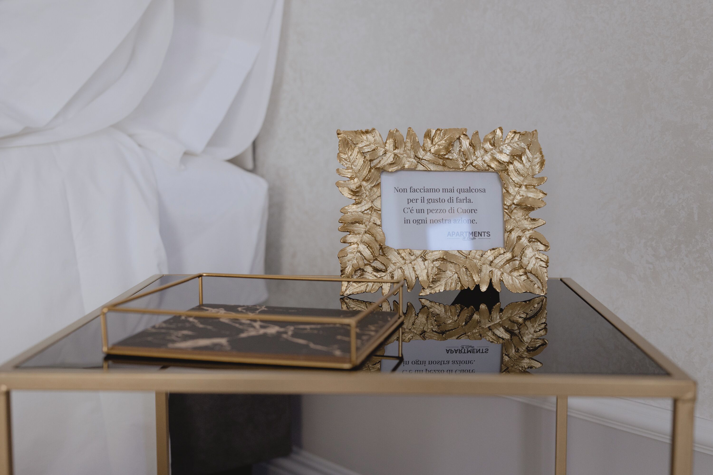 Een lijst met een citaat op een tafel, met een bladgouden ontwerp, een klein rechthoekig voorwerp en een label met de tekst 'APARTMENTS'.