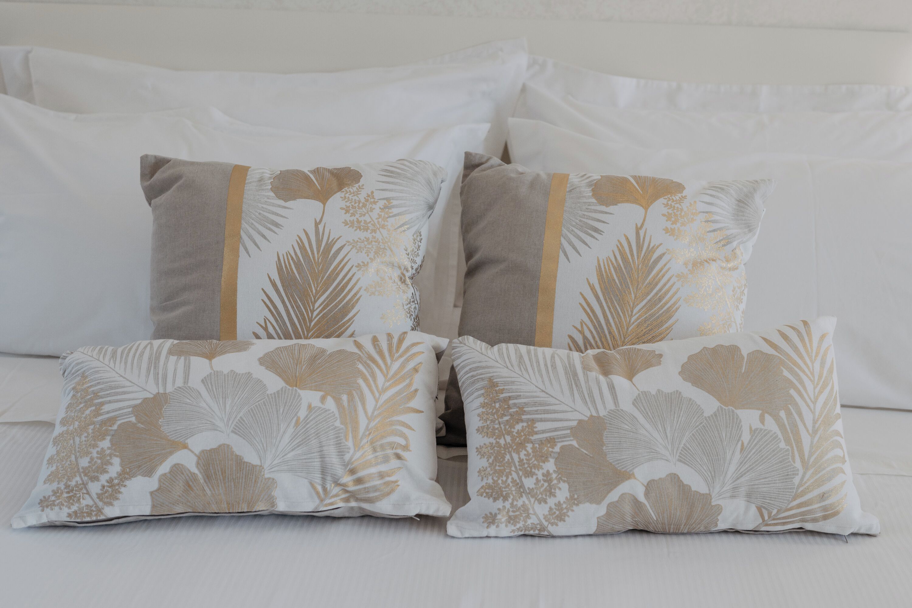 Een bed met witte beddengoed en decoratieve kussens met een bladmotief.
