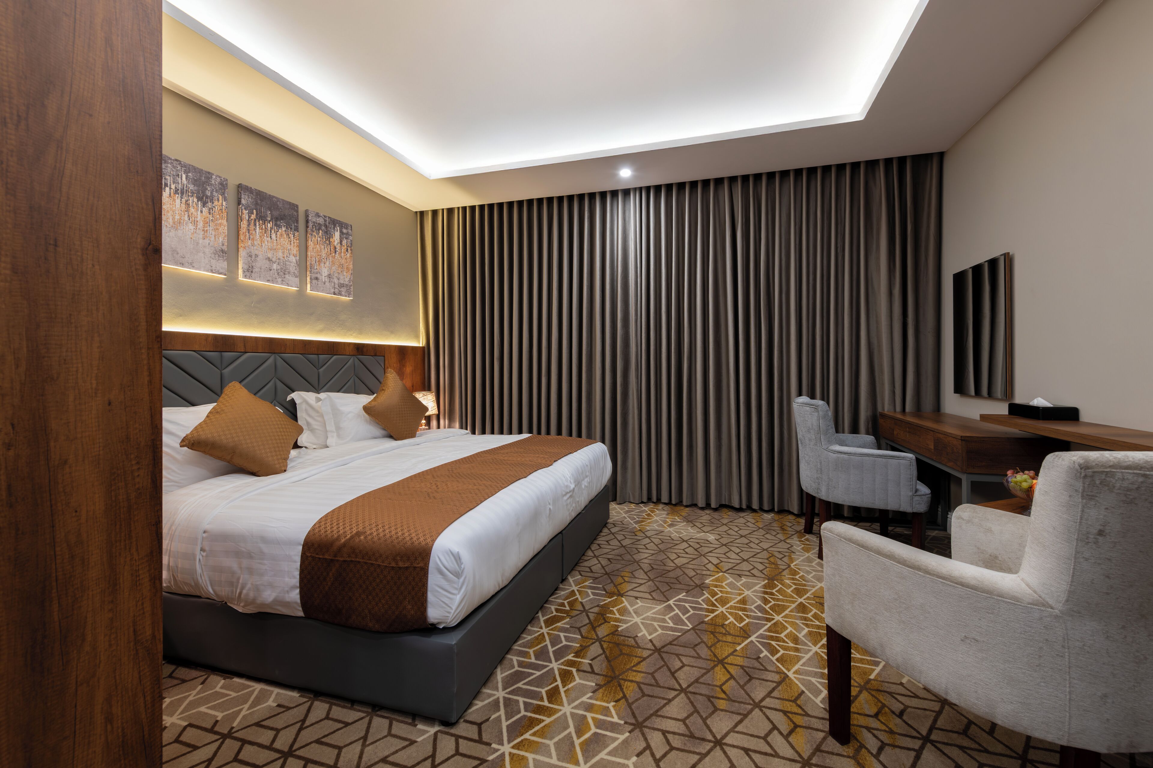A modern hotel room with a large bed, a desk, and a seating area.