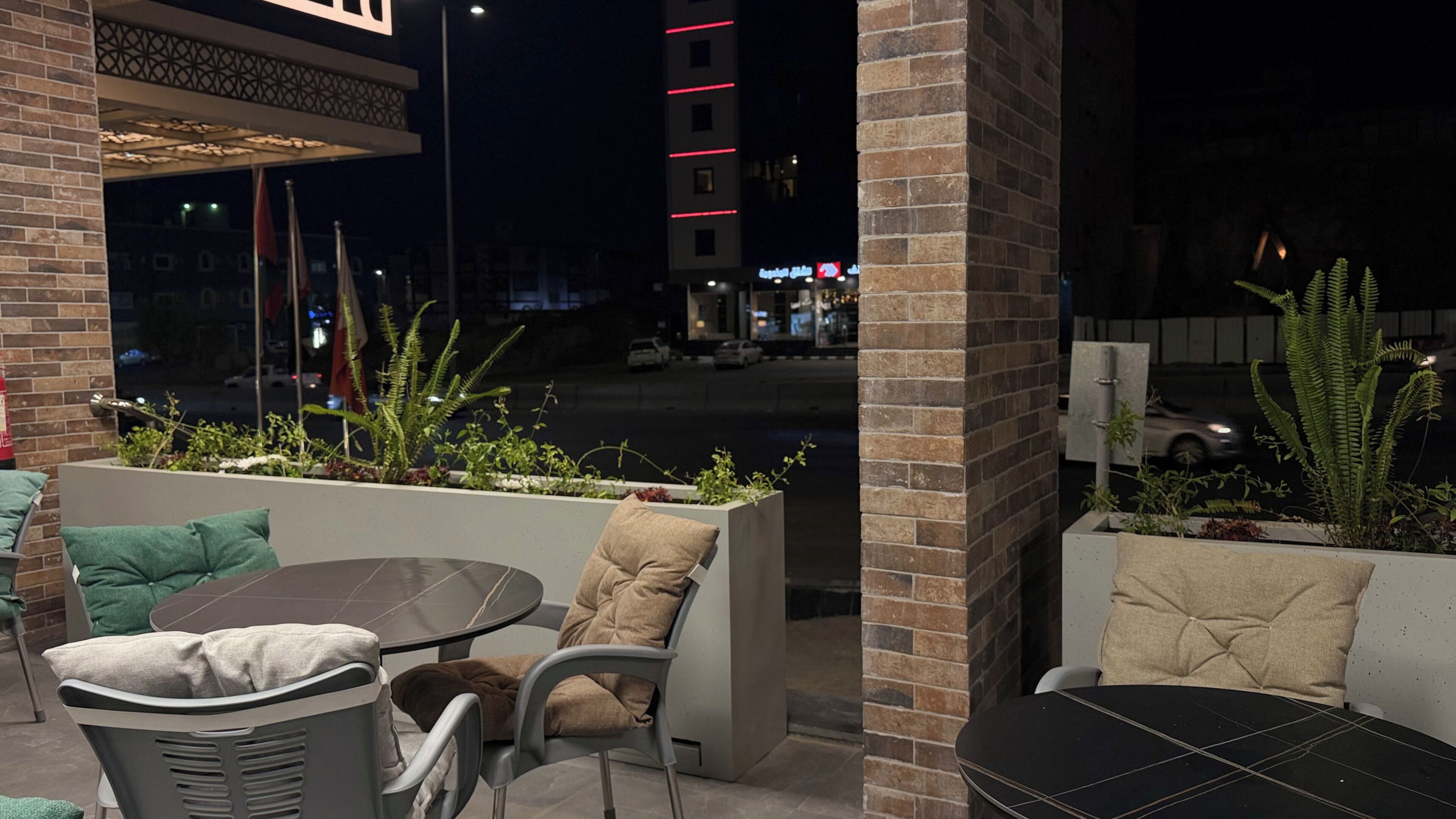 An outdoor seating area with chairs and tables, a brick wall, and a view of the street at night.