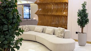 A modern living room with a curved sofa, decorative wall paneling, and a potted plant. - Armada Residence Hotel Apartments (Taif)