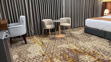 A hotel room with a bed, two chairs, a small table, and a patterned floor.