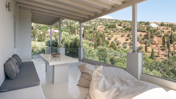Una habitación moderna con un ventanal amplio, un sofá, una mesita y vistas a un paisaje montañoso.