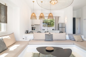 Un salon moderne avec un canapé, une table basse, des luminaires suspendus et une vue sur la cuisine.