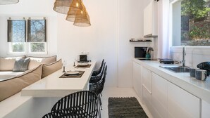Una cocina moderna con comedor, armarios blancos y un ventanal grande.