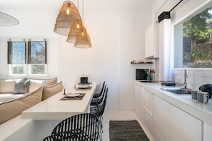 A modern kitchen with a dining area, white cabinetry, and a large window.