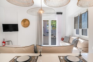 A modern living room with a dining area, a flat-screen TV, and a large window with curtains.