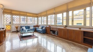 Un salón amplio con un ventanal grande, un sofá azul, una mesa de centro de vidrio y armarios de madera.