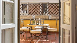 Un patio abierto con una mesa y sillas, una pared amarilla y una ventana con celosía metálica.