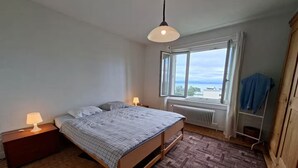 Ein Schlafzimmer mit einem Bett, zwei Nachttischlampen, einem Fenster mit Blick, einem Heizkörper und einem Holzschrank.