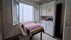 Ein kleiner, gut beleuchteter Raum mit Esstisch, Stühlen, einem Fenster und einer Küchenzeile.