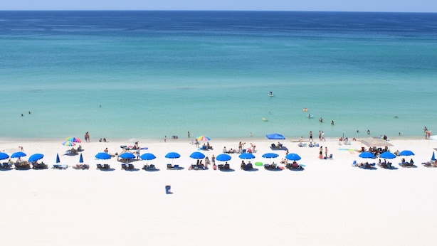 A beach with white sand and clear blue water. There are several blue umbrellas and lounge chairs. - Beachfront front Condo with Stunning Views & Last-Minute August Discounts! (Panama City Beach)