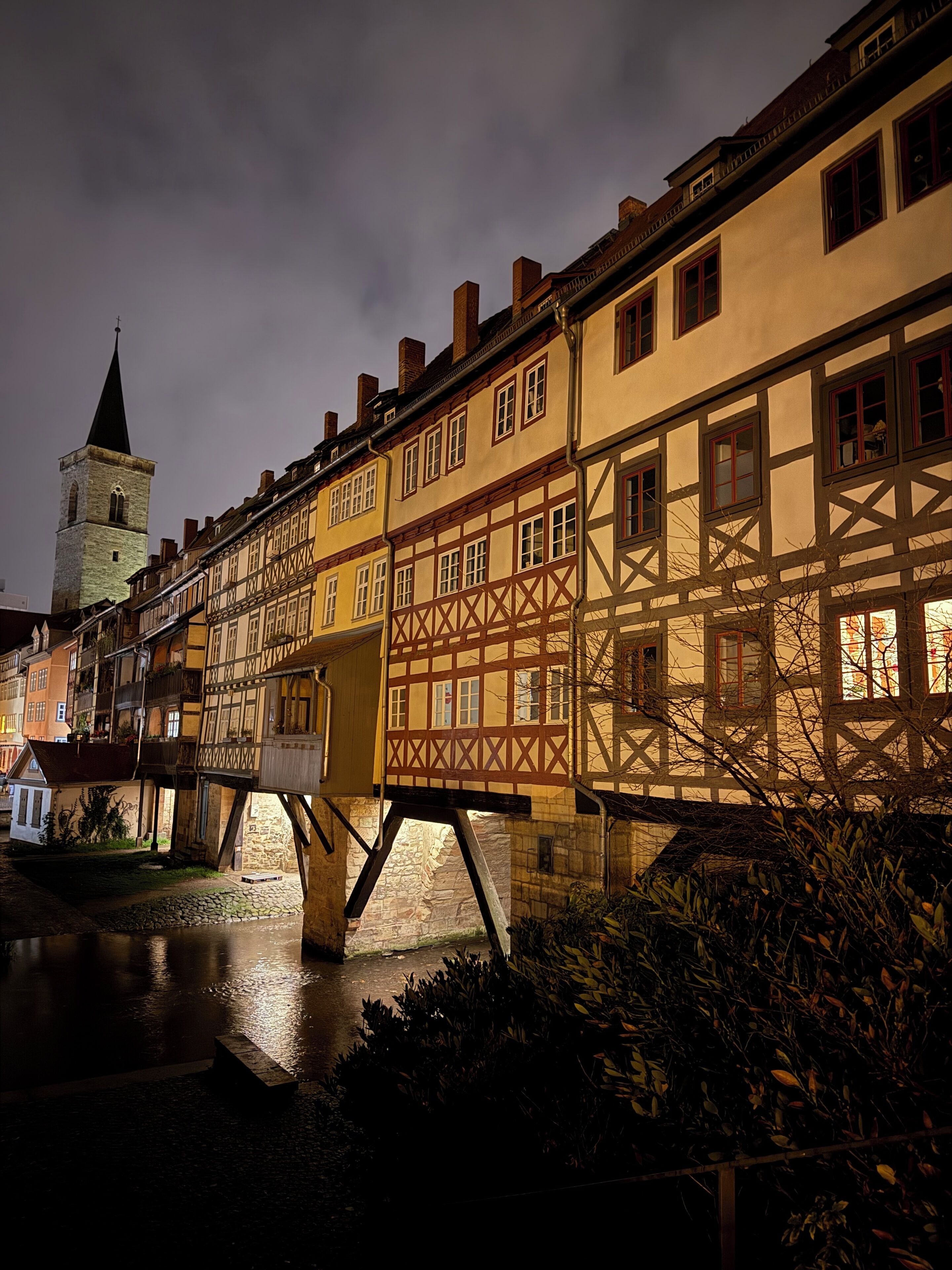 A historic building with a traditional half-timbered facade, a waterway in front, and a tower in the background.