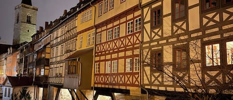A historic building with a traditional half-timbered facade, a waterway in front, and a tower in the background.