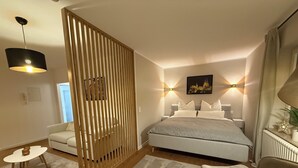 A modern bedroom with a bed, bedside tables, a chair, a desk, a decorative screen, and a painting on the wall. - Our new and cozy Krämernest in the old town, 100m to the Krämerbrücke (Erfurt)