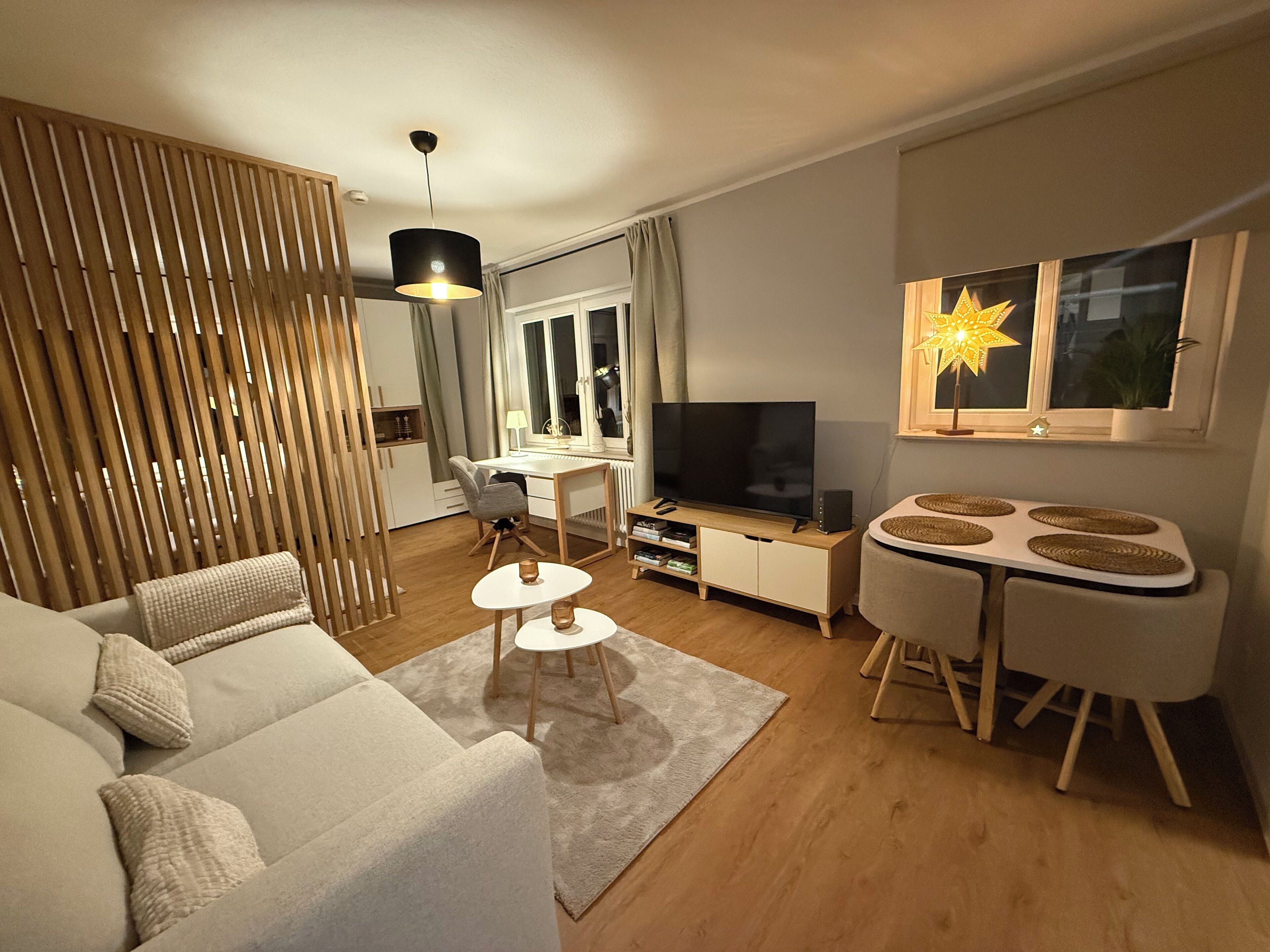 Ein modernes Wohnzimmer mit einer Couch, einem Esstisch, einem Fernseher und einer dekorativen Sternlampe.